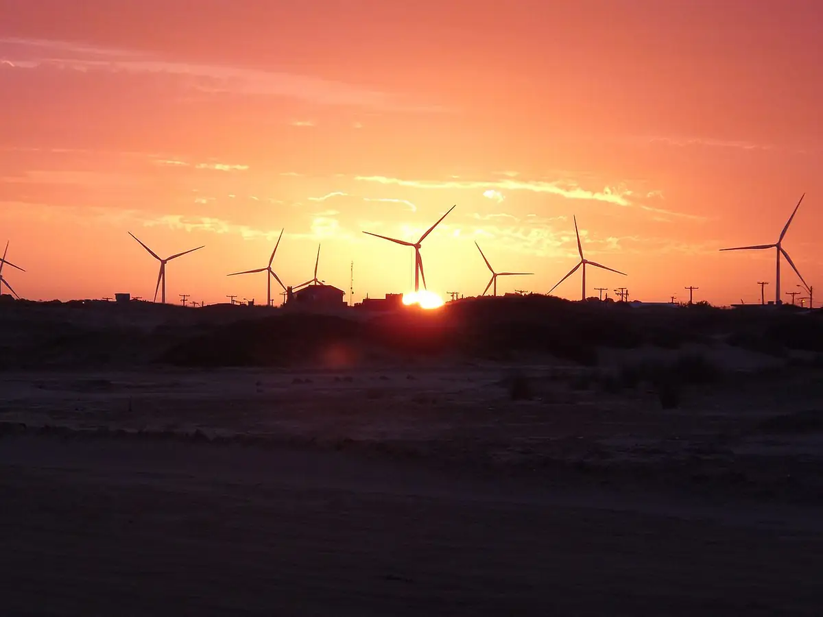Pôr do sol alaranjado atrás de aerogeradores, sobre dunas e areia da Praia do Cassino