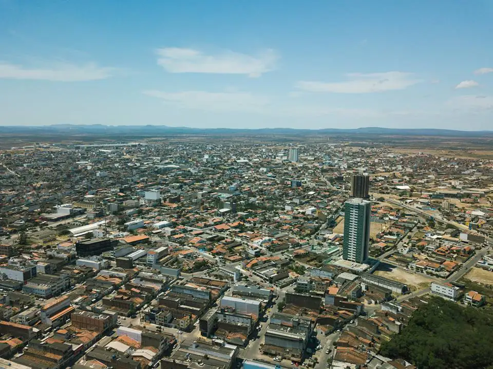 Vista aérea de Santa Cruz do Capibaribe, com telhados e prédios sob céu azul e terreno seco ao fundo