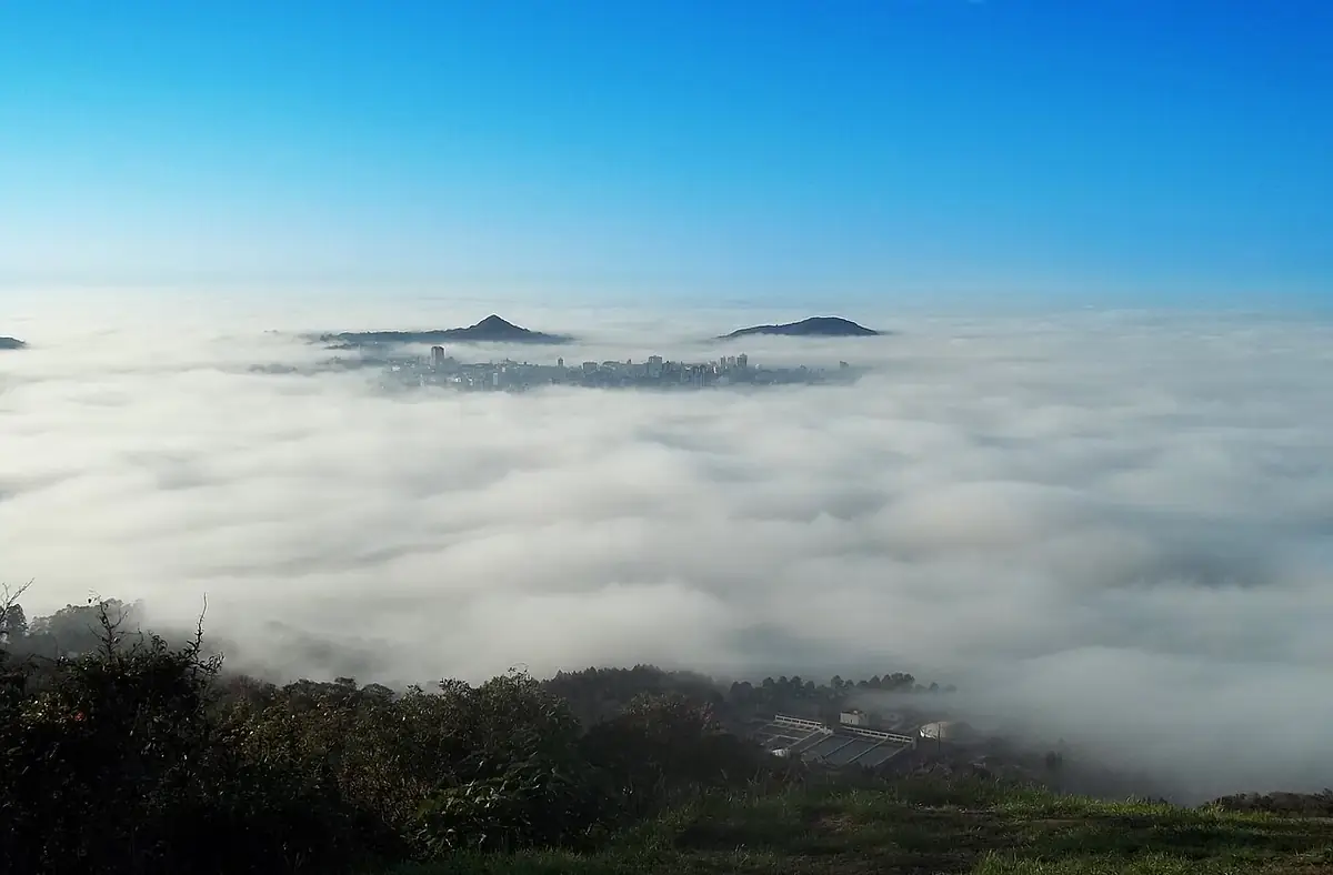 Cerração densa cobrindo a cidade de Santa Maria, com só os prédios do centro e dois morros acima das nuvens baixas
