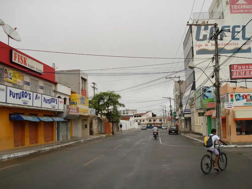 Rua Tiradentes, no centro de Santo Antônio de Jesus, com asfalto molhado e céu cinzento e nublado