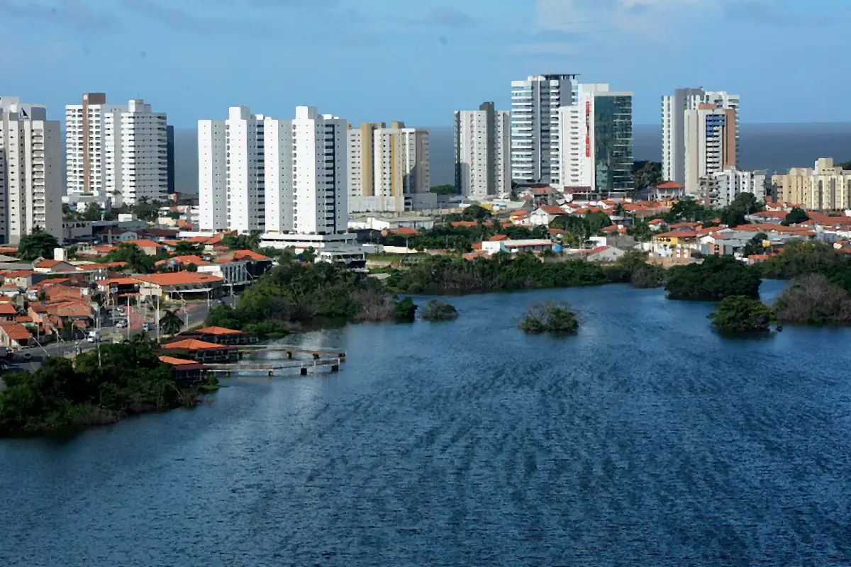 Lagoa da Jansen com mangue nas margens, prédios ao fundo e o mar no horizonte, sob céu com nuvens