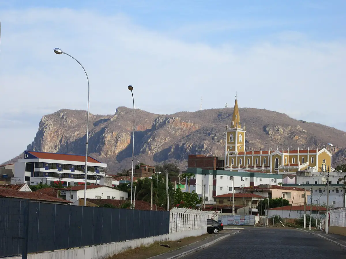 Igreja e a serra de paredão rochoso ao fundo, em Serra Talhada, sob céu com nuvens finas