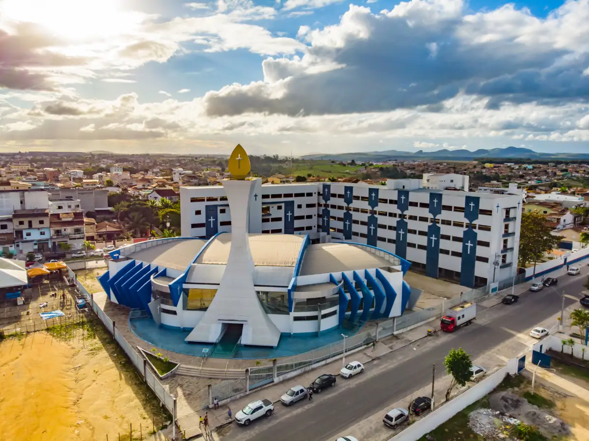 Catedral São Pedro e casas de Teixeira de Freitas vistas do alto, com nuvens carregadas e morros ao fundo