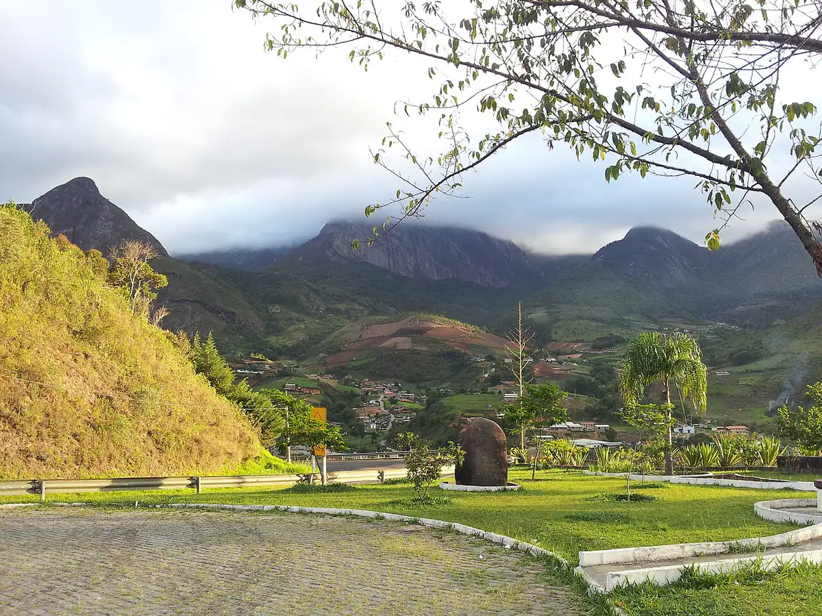 Picos rochosos da serra com as nuvens baixas encobrindo o topo, sobre um vale com casas e plantações em Teresópolis