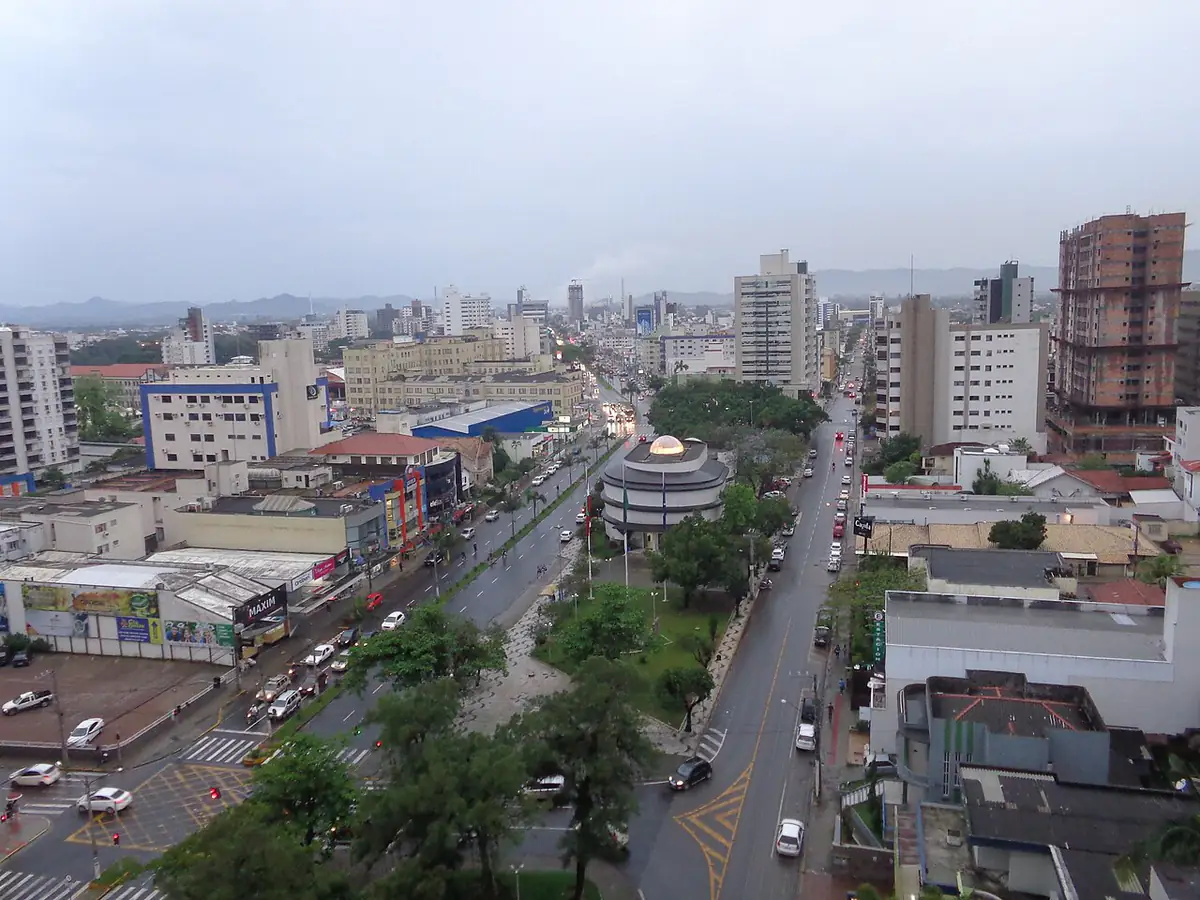 Avenida central de Tubarão em fim de tarde nublado, com ruas molhadas, o Museu Willy Zumblick ao centro e morros ao fundo
