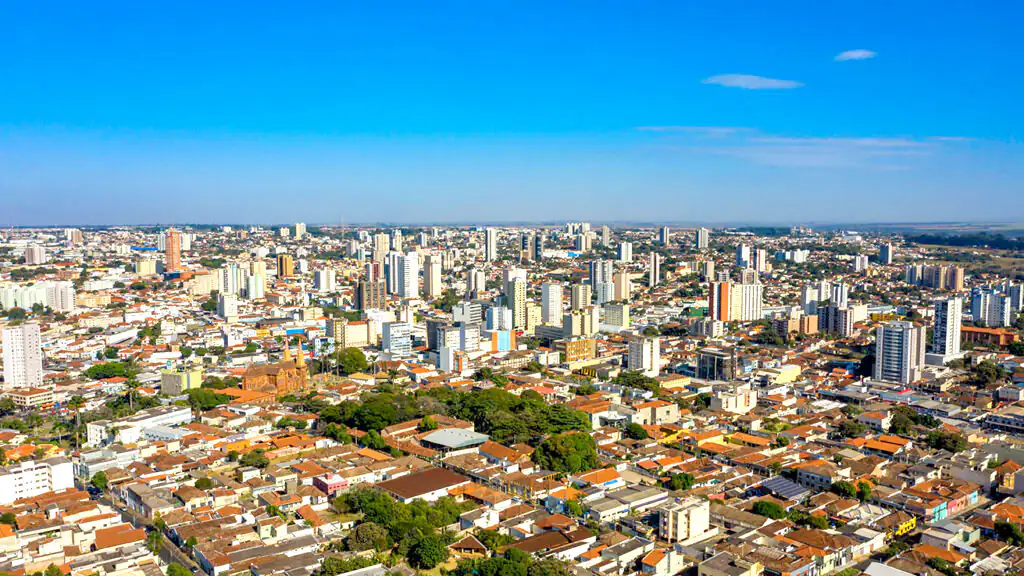 Vista aérea do centro de Uberaba (MG), com prédios, casas de telhado colonial e áreas verdes, sob céu azul com poucas nuvens.