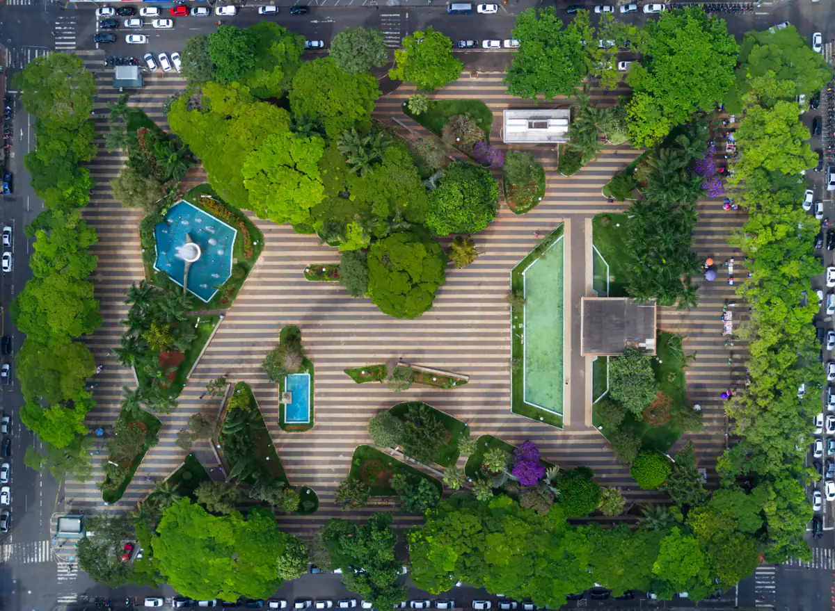 Vista aérea vertical da Praça Tubal Vilela, no centro de Uberlândia, com canteiros, árvores, fontes e espelhos d'água cercados por avenidas com carros estacionados.