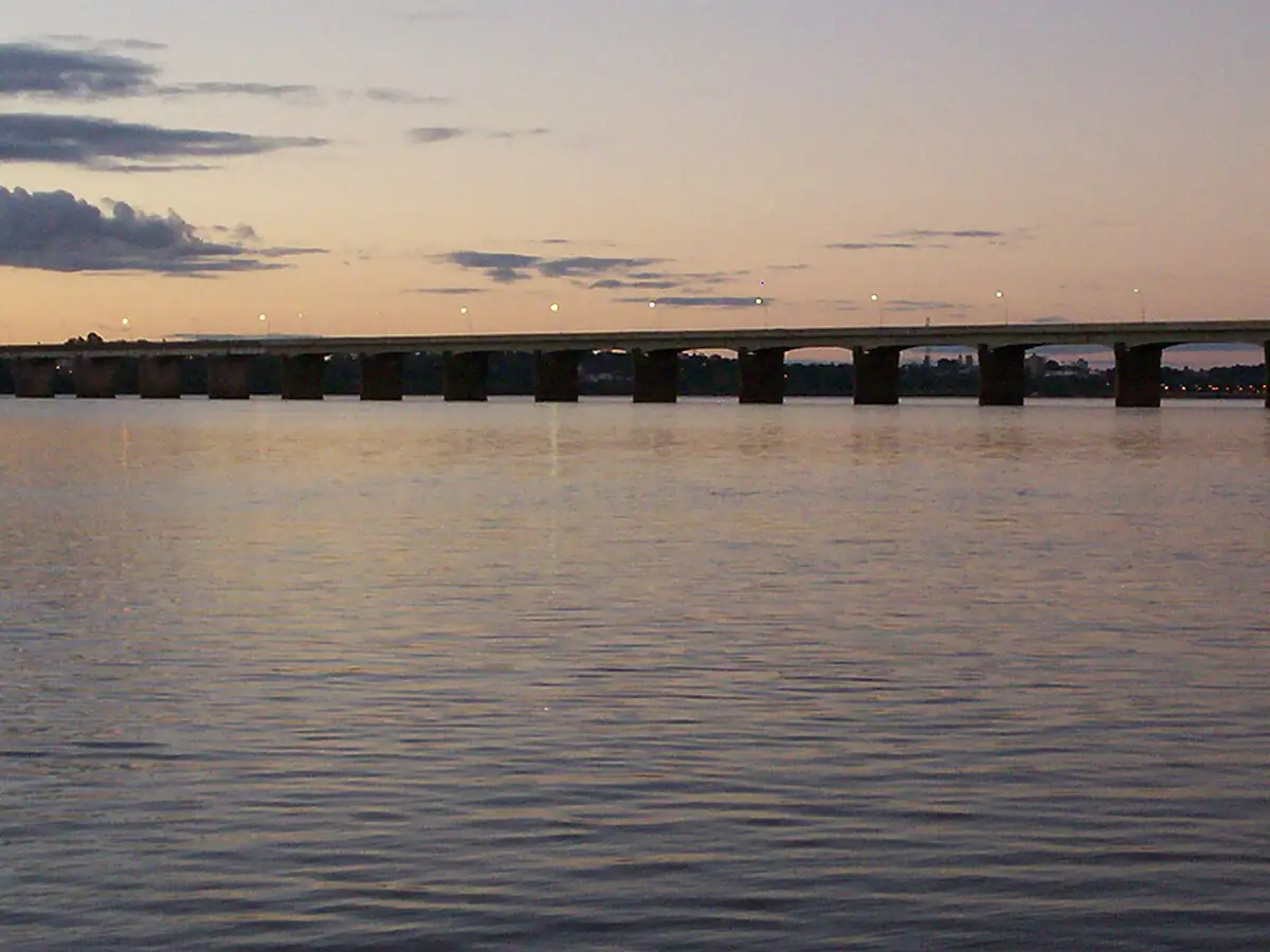 Rio Uruguai ao entardecer, com a ponte internacional entre Uruguaiana e Paso de los Libres ao fundo e nuvens no céu