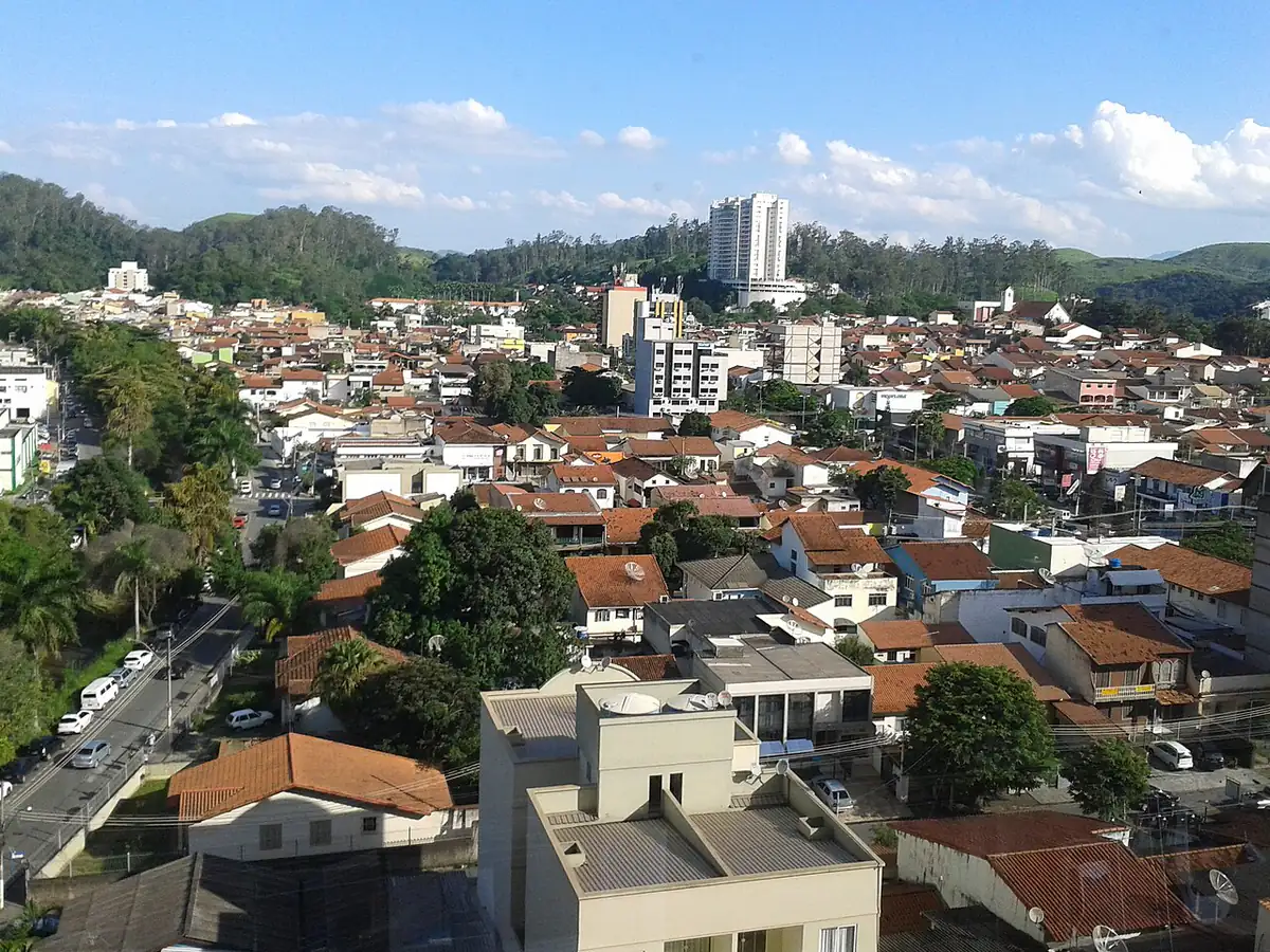 Vista de bairros de Volta Redonda com telhados e prédios, e morros cobertos de mata ao fundo sob céu azul